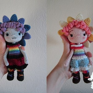 May include: Two crocheted dolls with rainbow striped shirts and flower-shaped hair. The doll on the left has purple and blue hair, a red and black dress, and brown boots. The doll on the right has pink and yellow hair, a blue skirt, and brown boots.