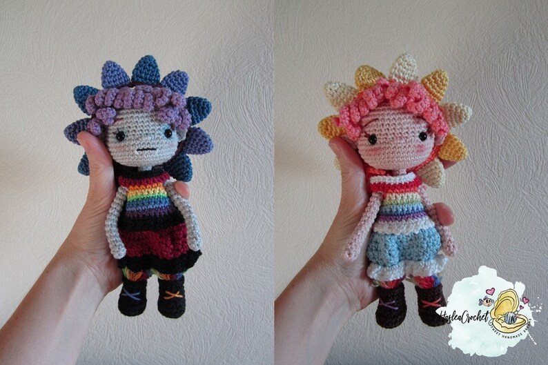 May include: Two crocheted dolls with rainbow striped shirts and flower-shaped hair. The doll on the left has purple and blue hair, a red and black dress, and brown boots. The doll on the right has pink and yellow hair, a blue skirt, and brown boots.