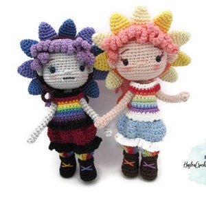 May include: Two crocheted dolls with rainbow striped tops and flower-shaped hair. The doll on the left has purple hair and a red skirt. The doll on the right has pink hair and a blue skirt.