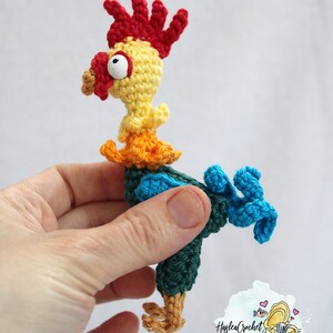 May include: A crocheted rooster toy with a red comb, yellow body, orange and blue accents, and a single large eye.