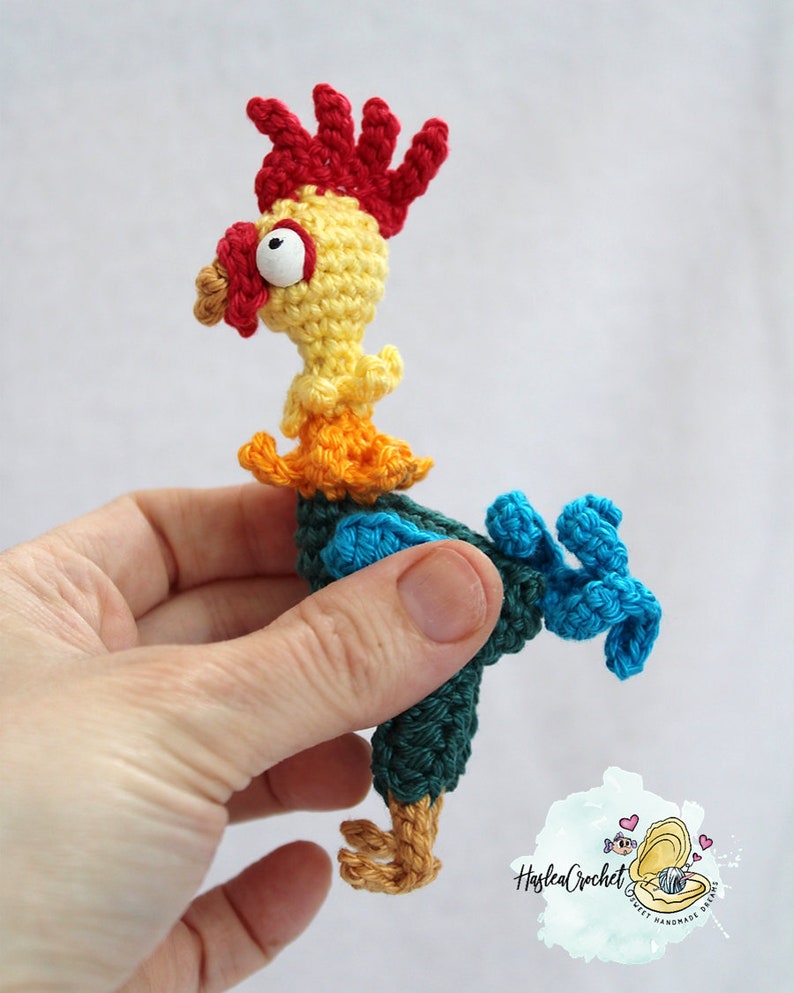 May include: A crocheted rooster toy with a red comb, yellow body, orange and blue accents, and a single large eye.