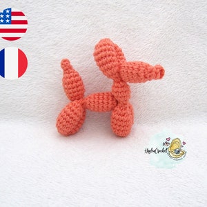 Puede incluir: Un animal de globo de crochet con forma de perro. El perro es de color naranja claro y está acostado sobre una superficie blanca y esponjosa.