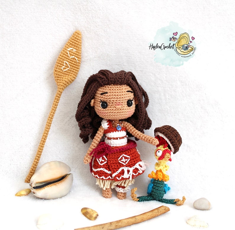 May include: Crocheted amigurumi doll of Moana from Disney's Moana, wearing a red and white dress with a brown and yellow rooster amigurumi toy. The doll has brown hair and brown eyes. The doll is holding the rooster toy in its right hand.