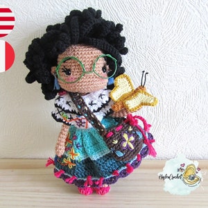 Puede incluir: Muñeca de crochet con piel marrón, cabello negro rizado y gafas que lleva un vestido colorido y lleva una mariposa y una pequeña bolsa.