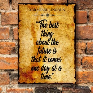 May include: A framed quote by Abraham Lincoln, "The best thing about the future is that it comes one day at a time," against a textured, aged paper background. The quote is set against a backdrop of a weathered brick wall.