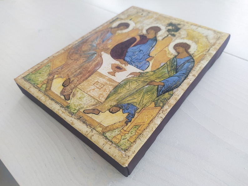May include: A religious icon depicting three figures in a seated pose, with a golden background and intricate details. The figures are dressed in colorful robes and have halos above their heads.