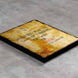 Peut inclure: Un parchemin jauni avec une citation de la série télévisée Game of Thrones. La citation dit "Quand on joue au jeu des trônes, on gagne ou on meurt." La citation est attribuée à Cersei Lannister.