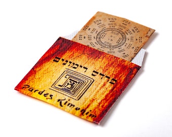 May include: A small, orange and yellow envelope with the text "Pardes Rimonim" and Hebrew text. The envelope is open and a small, brown paper with Hebrew text and a circle diagram is visible inside.