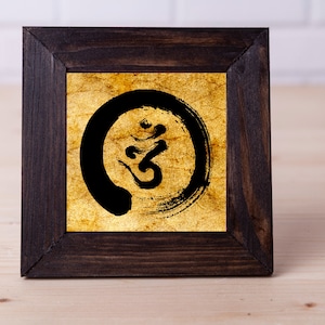 Può includere: Una stampa incorniciata di un simbolo Om in bianco e nero su sfondo dorato. Il simbolo Om è circondato da un cerchio.