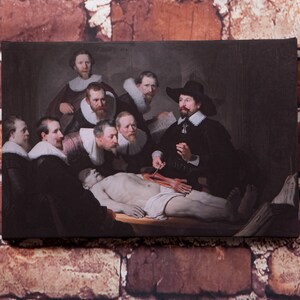May include: A painting depicting a group of men gathered around a table, observing a dissected body. The men are dressed in 17th-century attire, and the scene is lit by a single light source. The painting is a classic example of Dutch Golden Age art.