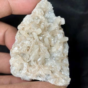 May include: A cluster of light beige crystals, possibly a mineral specimen, with a rough, textured surface. The crystals are tightly packed together, creating a visually interesting display. The overall shape is irregular, with a natural, unpolished appearance.