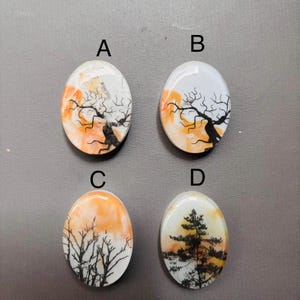 May include: Four oval-shaped resin cabochons with different tree silhouettes on a white background with orange and yellow watercolor washes. The trees are black.