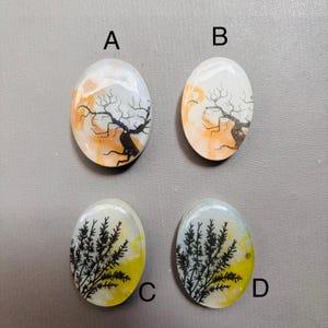 May include: Four oval-shaped agate cabochons with dendritic patterns. Two cabochons feature a black tree-like pattern on a white, orange, and brown background. The other two cabochons feature a black fern-like pattern on a white, yellow, and blue background.