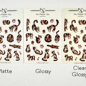 Puede incluir: Tres hojas de pegatinas con gatos calic&oacute; en varias poses. Las pegatinas est&aacute;n disponibles en acabados mate, brillante y brillante transparente. El texto en las hojas dice "Ink Paper. Go. - Calico Kitties - 2022 Ink Paper Go LLC."