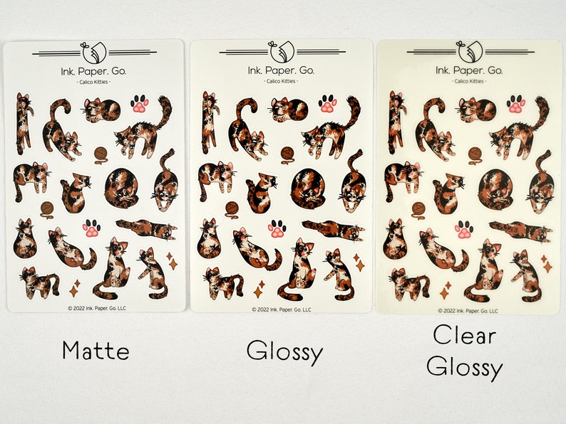 Puede incluir: Tres hojas de pegatinas con gatos calic&oacute; en varias poses. Las pegatinas est&aacute;n disponibles en acabados mate, brillante y brillante transparente. El texto en las hojas dice "Ink Paper. Go. - Calico Kitties - 2022 Ink Paper Go LLC."