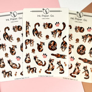 Puede incluir: Tres hojas de pegatinas con gatos calic&oacute; en varias poses. Las pegatinas son blancas con gatos calic&oacute; negros y naranjas. Las pegatinas tienen el texto "Ink. Paper. Go. - Calico Kitties" y "&copy; 2022 Ink Paper Go LLC".