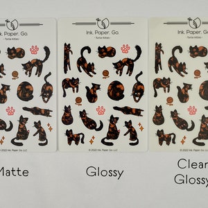 Op de afbeelding: Drie vellen met stickers met illustraties van schildpadkatten in verschillende poses. De stickers zijn gelabeld met "Mat", "Glans" en "Helder Glans". De tekst "Ink. Paper. Go. - Tortie Kitties" staat op elk vel.