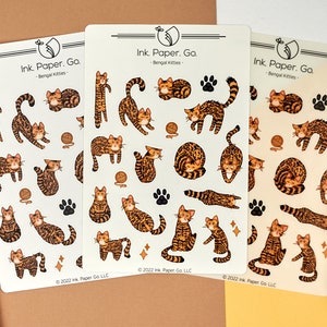 May include: Three sheets of stickers featuring illustrations of Bengal cats in various poses. The stickers are printed on white paper with a light beige background. The text "Ink. Paper. Go. - Bengal Kitties -" is printed at the top of each sheet. The copyright information "© 2022 Ink. Paper Go LLC" is printed at the bottom of each sheet.
