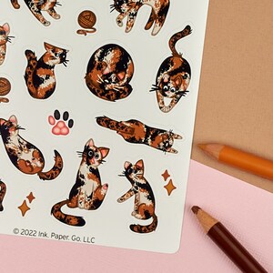 Puede incluir: Una hoja de pegatinas con una variedad de adorables gatos calic&oacute; en diferentes poses. Las pegatinas est&aacute;n sobre un fondo blanco con un aviso de copyright en la parte inferior que dice "2022 Ink. Paper. Go. LLC."