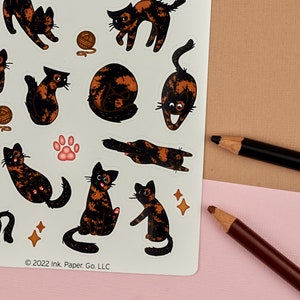 Op de afbeelding: Een vel stickers met verschillende schattige calico katten in verschillende poses. De stickers zijn gedrukt op wit papier en hebben een glanzende afwerking. Het vel bevat ook een pootprint en een paar sterren.