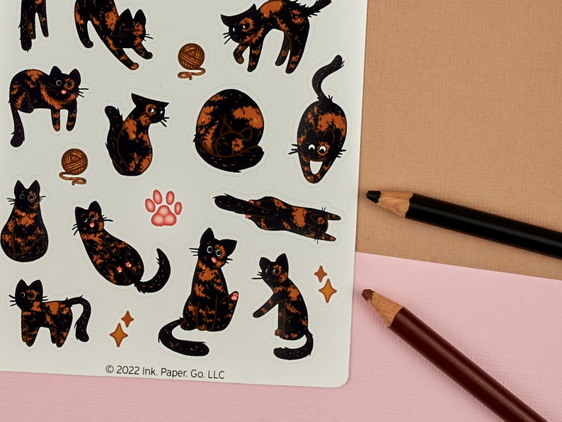 Op de afbeelding: Een vel stickers met verschillende schattige calico katten in verschillende poses. De stickers zijn gedrukt op wit papier en hebben een glanzende afwerking. Het vel bevat ook een pootprint en een paar sterren.