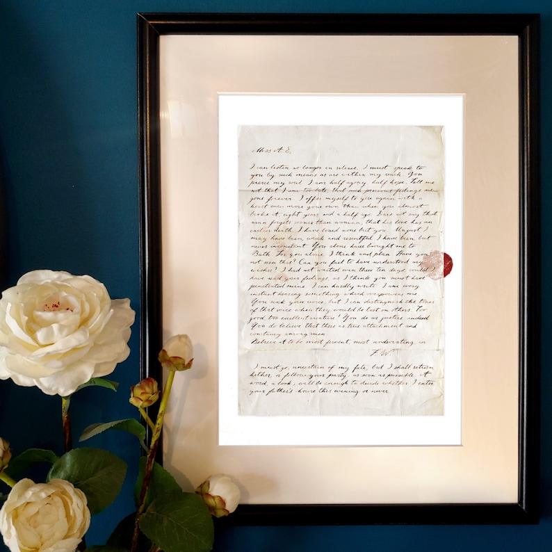 May include: A framed letter written in cursive script on aged paper. The letter is a personal correspondence with a handwritten seal in the bottom right corner. The letter is displayed against a dark blue wall with white flowers.