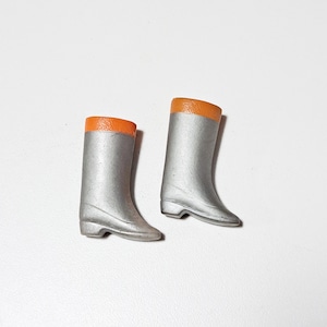 May include: A pair of miniature silver boots with orange tops. The boots have a classic design, with a rounded toe and a small heel. The boots are made of a smooth material and are set against a white background.
