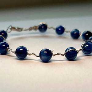 May include: A blue gemstone bracelet with silver wire wrapping each bead.