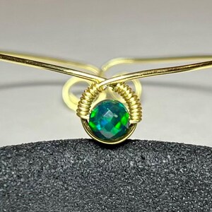 May include: A gold wire wrapped bracelet with a green opal gemstone in the center.