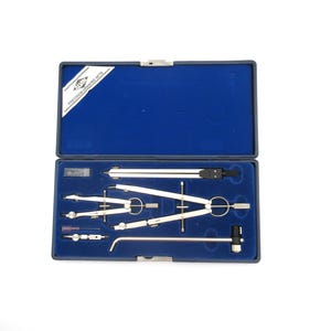 May include: A blue case containing a precision drawing set. The set includes various silver-colored compasses, dividers, and a technical pen. The case has a blue velvet lining and a label that reads "Precision Drawing Sets".
