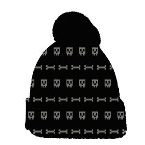 May include: A black knit beanie featuring a pom-pom on top and a repeating pattern of grey pixelated skulls and bones. The hat has a folded cuff at the bottom, and the design is arranged in alternating horizontal rows across the entire surface.