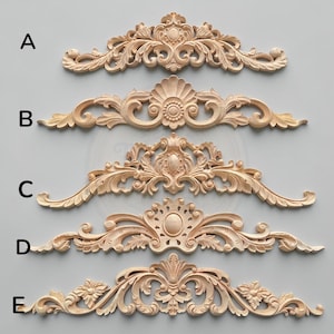 May include: Five light-coloured wooden decorative carvings labelled A through E, each featuring intricate symmetrical scrollwork, floral motifs, and central oval or shell-shaped elements. These horizontal wood appliqués display detailed relief carvings.