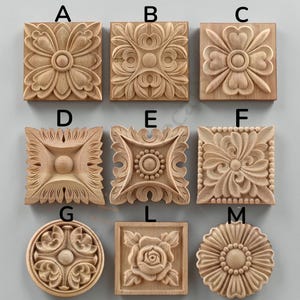 May include: A collection of nine light-coloured wooden decorative carvings labelled A through M. The pieces feature various relief patterns including floral, leaf, and geometric motifs in square and circular shapes with detailed wood grain textures.