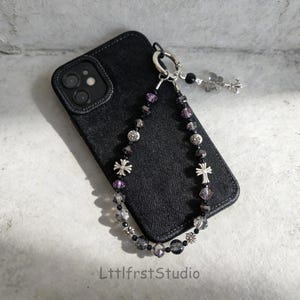 May include: Black denim phone case with a beaded strap featuring silver crosses, purple and clear beads. The strap is attached to the case with a silver ring. The text "LttlfstStudio" is at the bottom of the image.