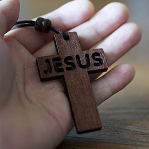 May include: A wooden cross necklace with the word "JESUS" carved into it. The cross is brown and has a dark brown cord.