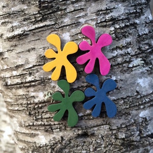 May include: Four wooden shapes in the form of abstract flowers, painted in yellow, pink, green, and blue, are arranged on a tree trunk.