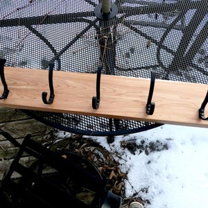 May include: A wooden coat rack with five black metal hooks. The rack is made of light-colored wood and is mounted on a metal table. The hooks are evenly spaced along the length of the wood.