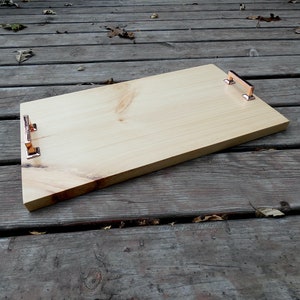May include: A rectangular wooden serving tray with copper-colored handles. The tray is made of light-colored wood and has a natural wood grain. The handles are rectangular and attached to the tray's short sides.