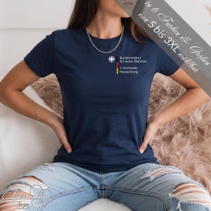 Könnte beinhalten: Dunkelblaues T-Shirt mit dem Text "Bundesinstitut für lecker Bierchen" und "1. Vorsitzende Nicola König" auf der Vorderseite. Das Shirt hat auch ein kleines Emblem mit den Farben der deutschen Flagge. Erhältlich in den Größen S bis 3XL.