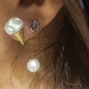 Puede incluir: Un par de pendientes con una perla blanca y un cono de helado blanco con una cadena dorada. El cono de helado est&aacute; coronado con una perla blanca. Los pendientes son usados por una persona con cabello oscuro.