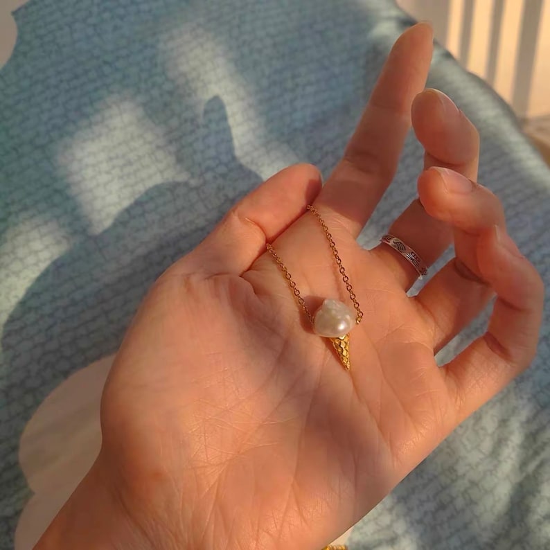 Puede incluir: Un collar de cadena dorada con un colgante de helado de oro y perla.