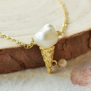 Puede incluir: Un collar de cadena dorada con un colgante con forma de perla que parece un cono de helado. El colgante est&aacute; hecho de metal dorado y tiene una superficie texturizada. La cadena est&aacute; hecha de peque&ntilde;as piezas de metal dorado unidas.