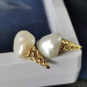 Puede incluir: Un par de pendientes de oro con perlas barrocas blancas con forma de conos de helado.