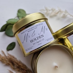 May include: A gold-coloured metal candle tin with a white label featuring the text "THANK YOU FOR BEING PART OF OUR WEDDING DAY", "Mr & Mrs", "HOLDEN", "24 | April | 23", and "mint & eucalyptus". The label also notes "3.5oz - 20 hr burn".
