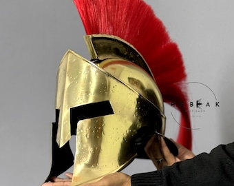 Peut inclure: Un casque spartiate en or avec une crinière de cheval rouge. Le casque a un masque facial noir et une mentonnière en cuir.