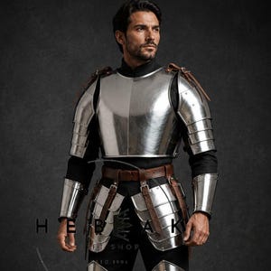 Op de afbeelding: Een volledig pak van gepolijst metalen harnas, inclusief borstplaat, schouderbeschermers, arm- en beenbescherming en een riem met leren riemen. Het harnas wordt gedragen over een zwarte outfit. De tekst "HEBAK SHOP" en "EST. 1994" is zichtbaar.