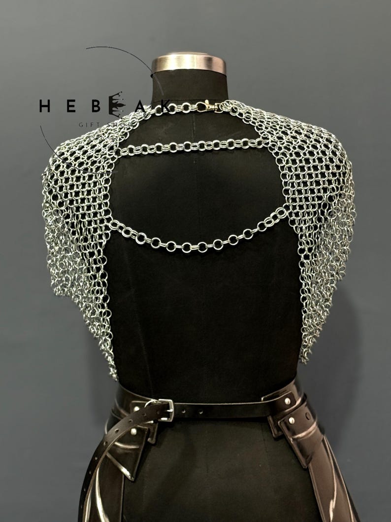 May include: A silver chainmail shoulder piece with a backless design. The chainmail is draped over a black mannequin, with a black leather belt and accents visible below. The image includes the text "HEBE GIFTS".