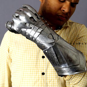 K&ouml;nnte beinhalten: Ein silberner Metallhandschuh mit einem klauenartigen Design und aufwendigen Gravuren. Der Handschuh wird am linken Arm einer Person getragen, die ein gelb-wei&szlig; kariertes Hemd tr&auml;gt.