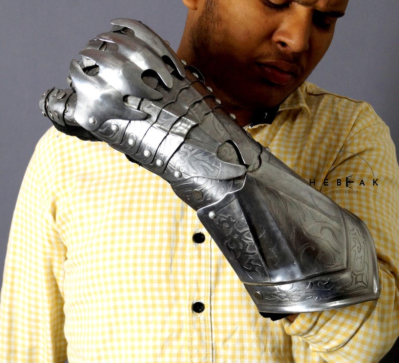 K&ouml;nnte beinhalten: Ein silberner Metallhandschuh mit einem klauenartigen Design und aufwendigen Gravuren. Der Handschuh wird am linken Arm einer Person getragen, die ein gelb-wei&szlig; kariertes Hemd tr&auml;gt.