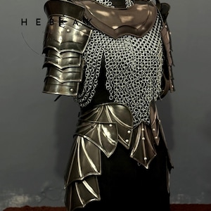 May include: A medieval-style armor set displayed on a mannequin. The armor features layered metal plates, chainmail, and leather accents. The design includes shoulder pauldrons, a chest plate, and a skirt-like lower section. The color palette is primarily metallic silver and dark brown.